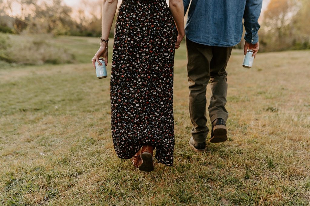 Closeup of couple walking together on grassy field with beer in their hands
