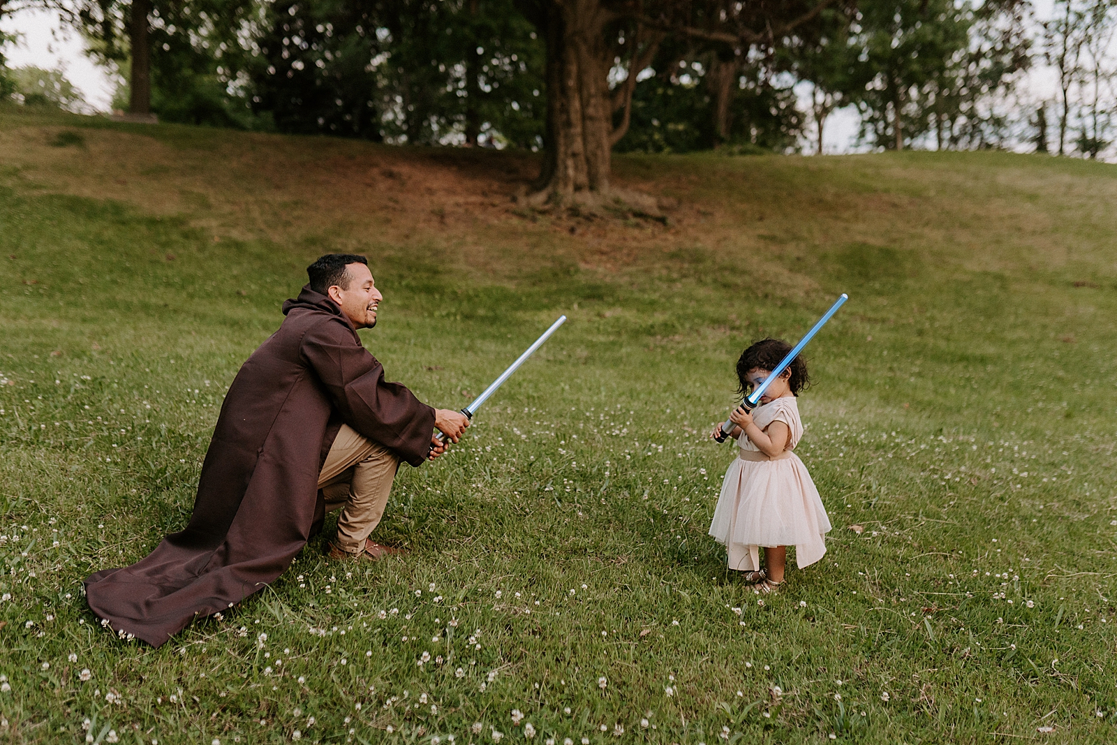 Father and daughter holding lightsabers on grassy field playing