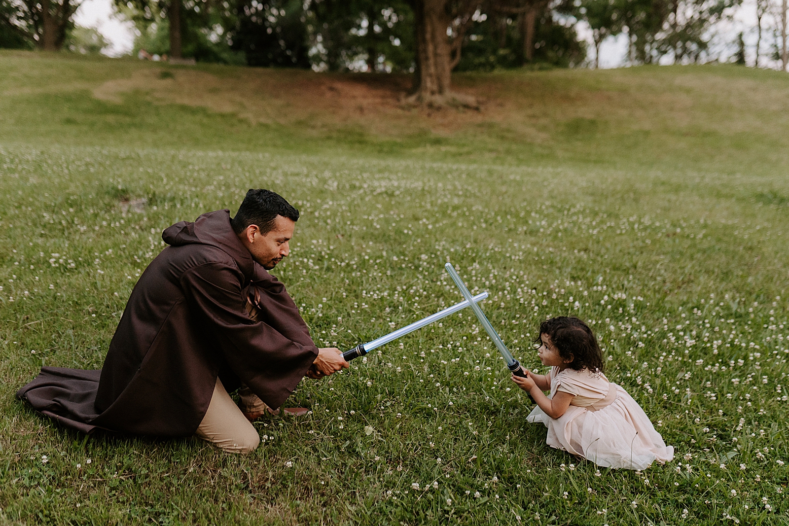 Father and daughter clashing lightsaber on grassy field