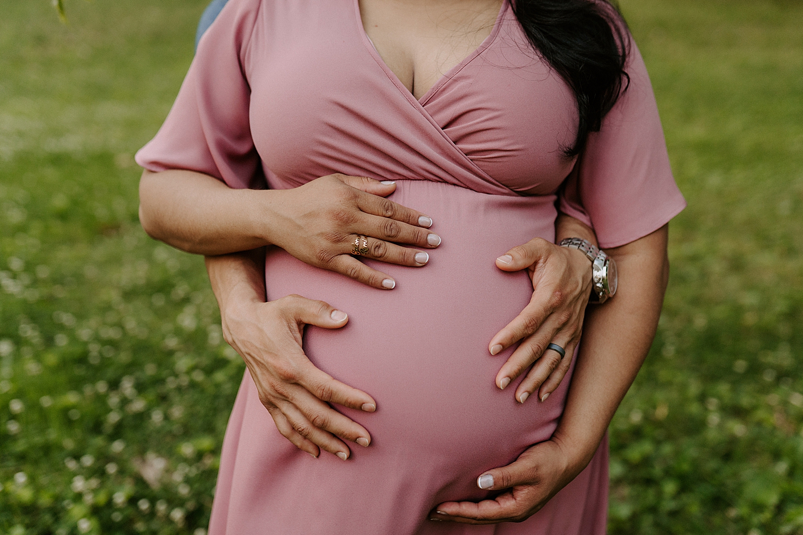 Closeup of couple holding baby bump on grassy field