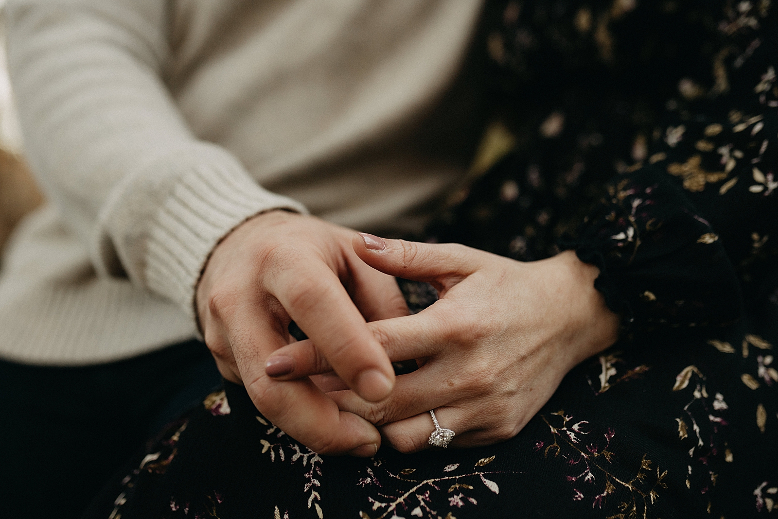 Closeup of couple holding hands on lap with engagement ring
