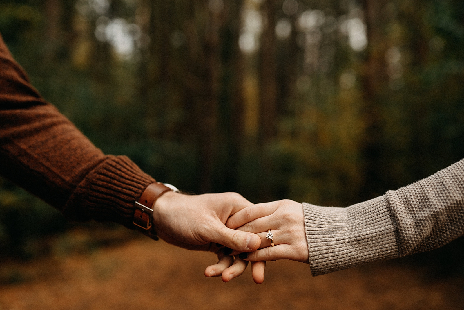 Closeup of couple extending their arms out to hold hands with emphasis of engagement ring