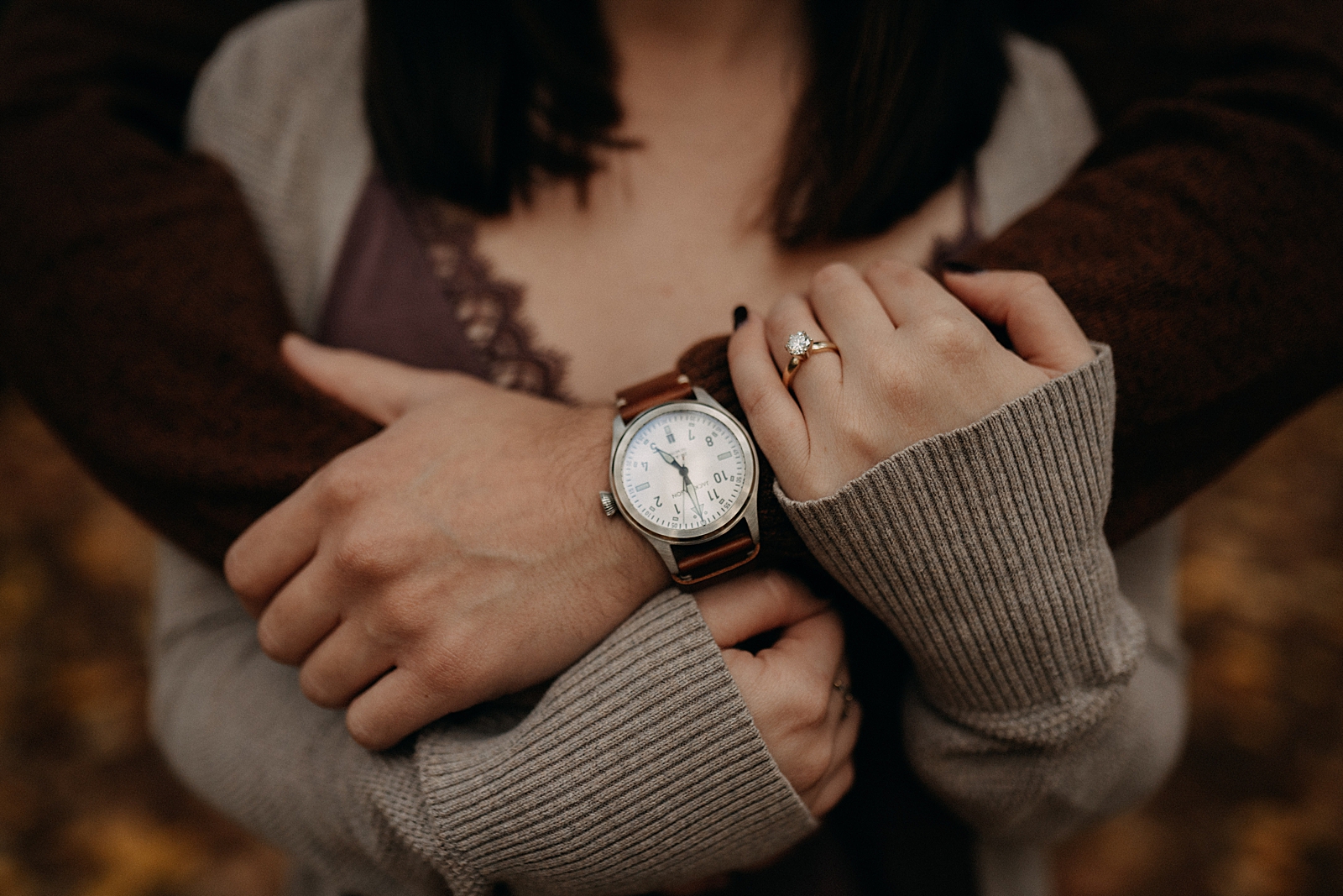 Closeup of man holding woman with watch on and engagement ring
