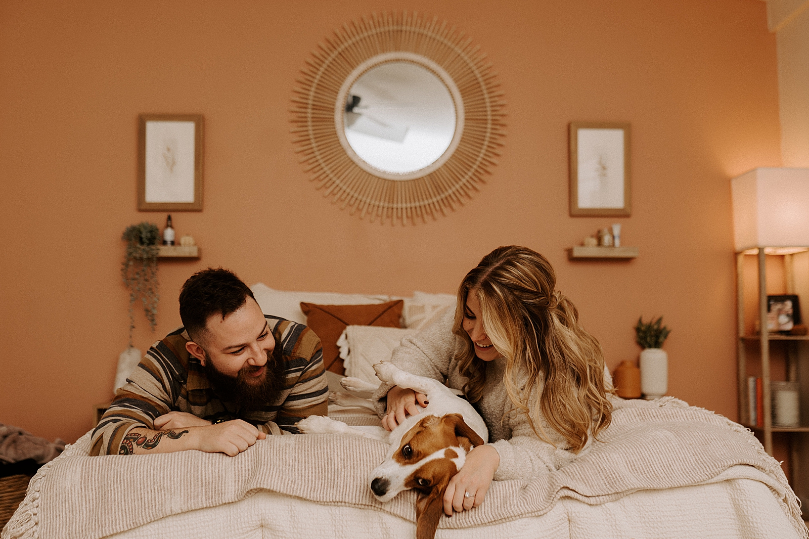 Couple laying down on end of bed playing with dog in the middle