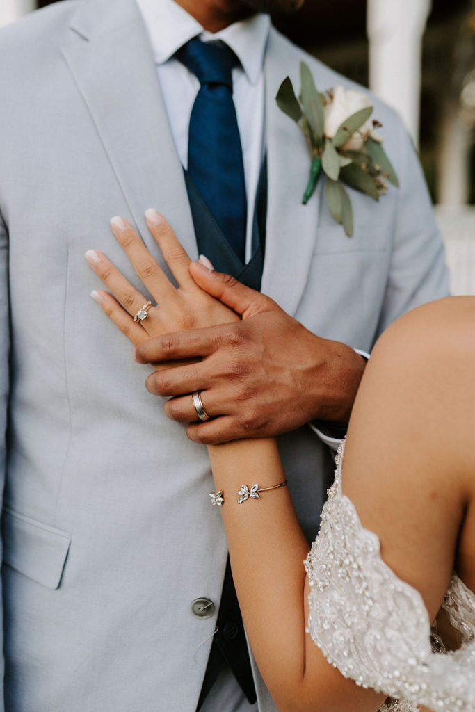 Closeup of Bride's hand on Groom's chest with wedding bands and engagement ring on