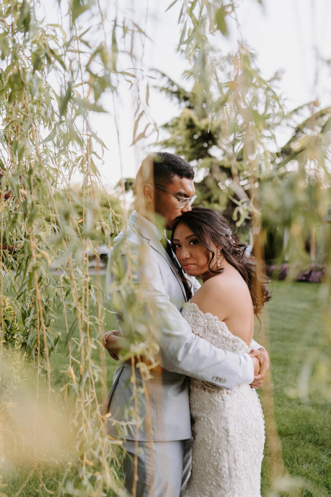 Bride and Groom hugging each other with green vines in front of camera