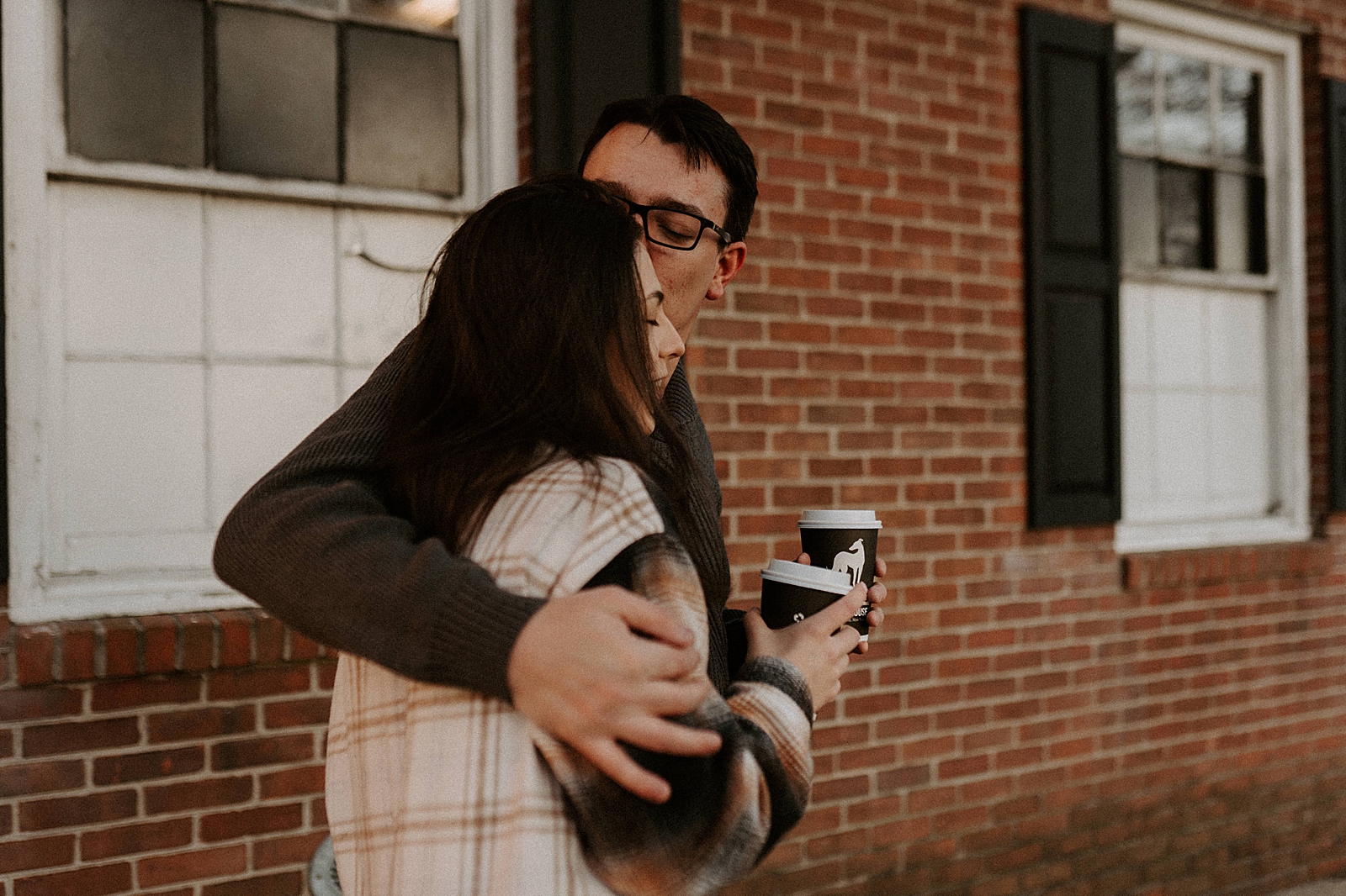 Man holding woman from the side and kissing head with coffees in hand