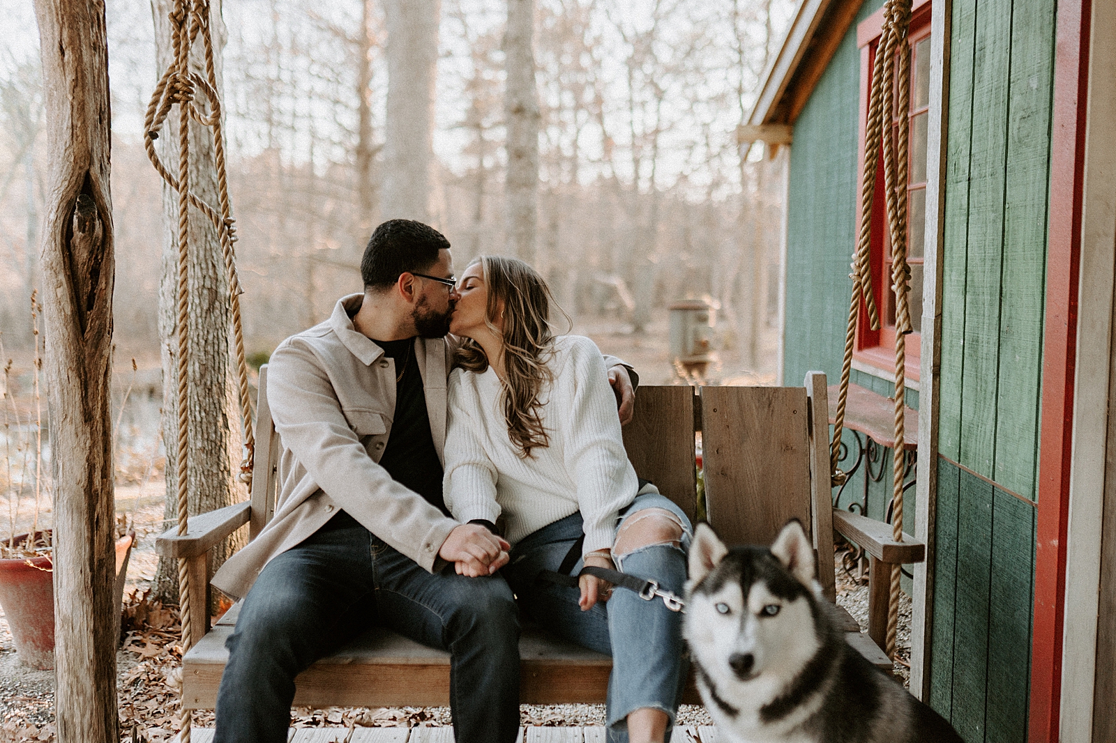 Couple sitting on swinging bench and kissing with Husky